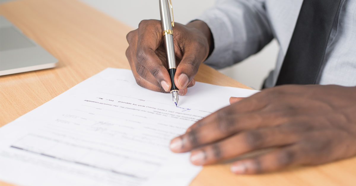 Person Signing a Document on a Wooden Desk with a Silver Fountain Pen