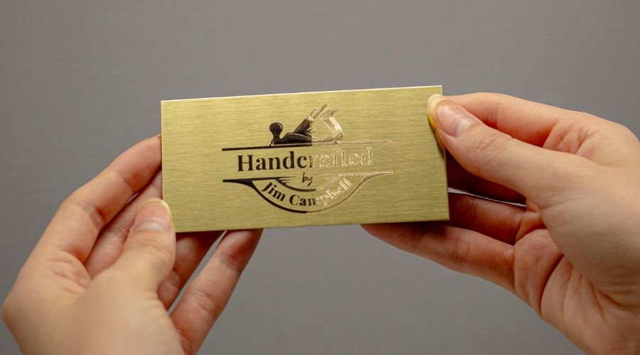 A person holding an engraved brass sign that is half oxidized