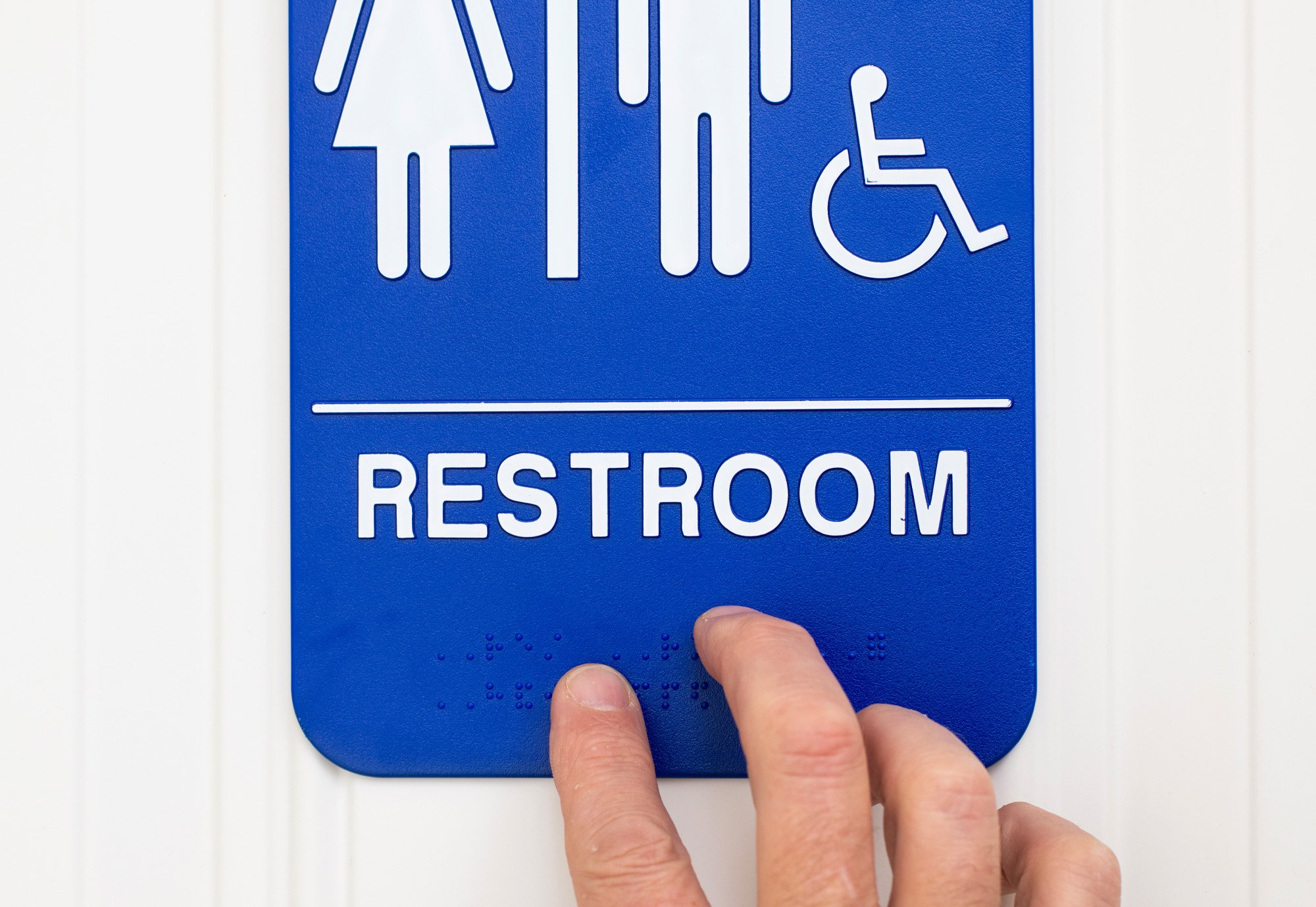 A Person's Hand Touching Braille on an ADA Sign